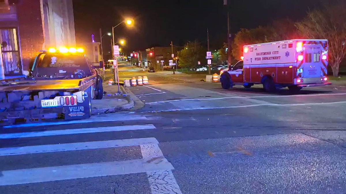 One of multiple ambulances is leaving the site of a vehicle collision that has damaged two houses in East Baltimore