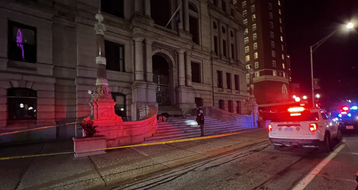 Crime scene tape surrounds the staircase at the front of Providence City Hall. Detectives are currently on scene investigating a reported stabbing. A bicycle and other belongings are scattered across the stairs, facing Kennedy Plaza