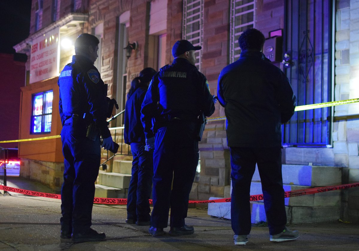 A trio of officers walk homicide detective Michael Frey through the site of a fatal shooting in southwest Baltimore. A 50-year-old man was critically injured by gunfire. He died at a local hospital, according to police
