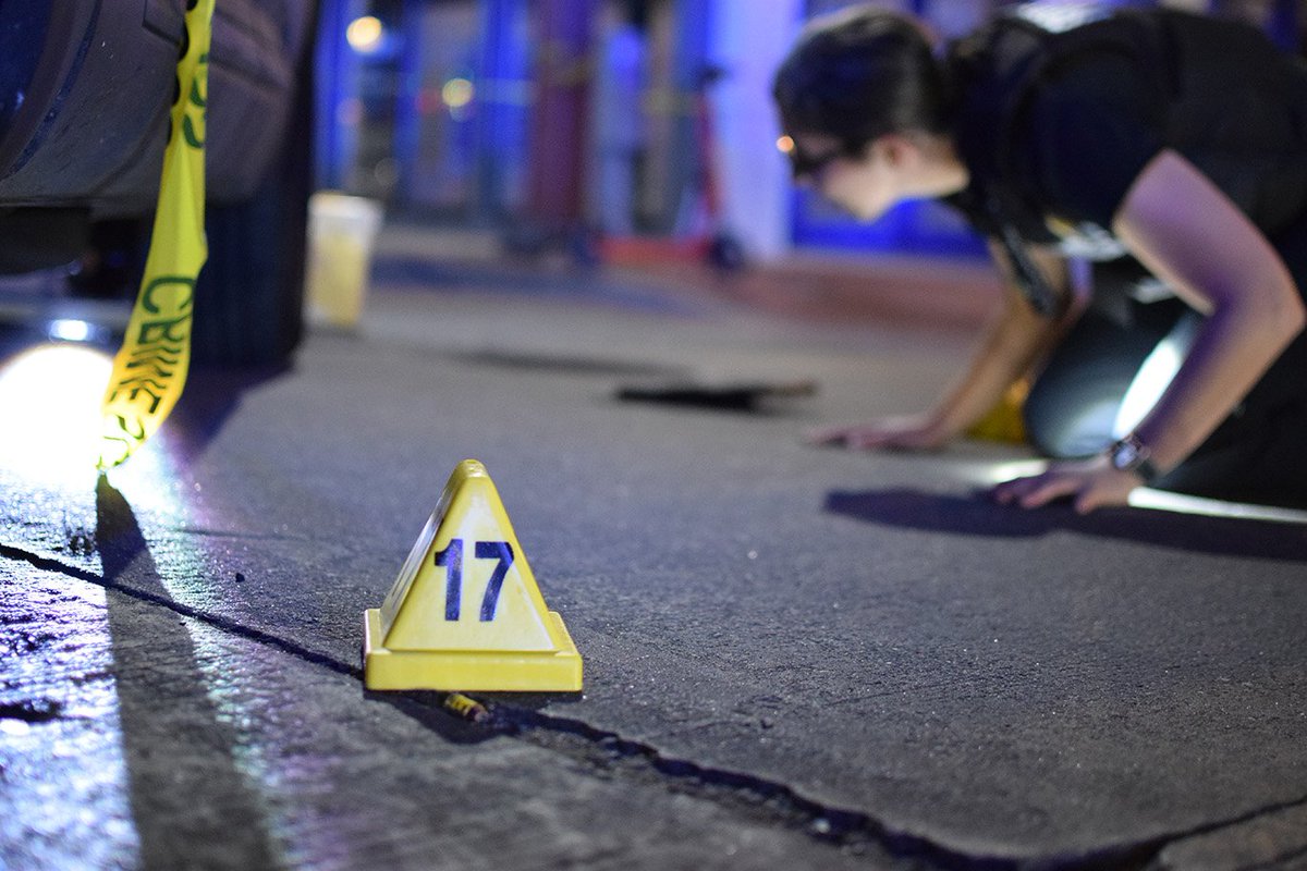 A crime lab technician searches for cartridge casings following a bout of gunfire in Fells Point. Police heard bullets flying through the southeast neighborhood around 12:15 a.m. on Saturday.